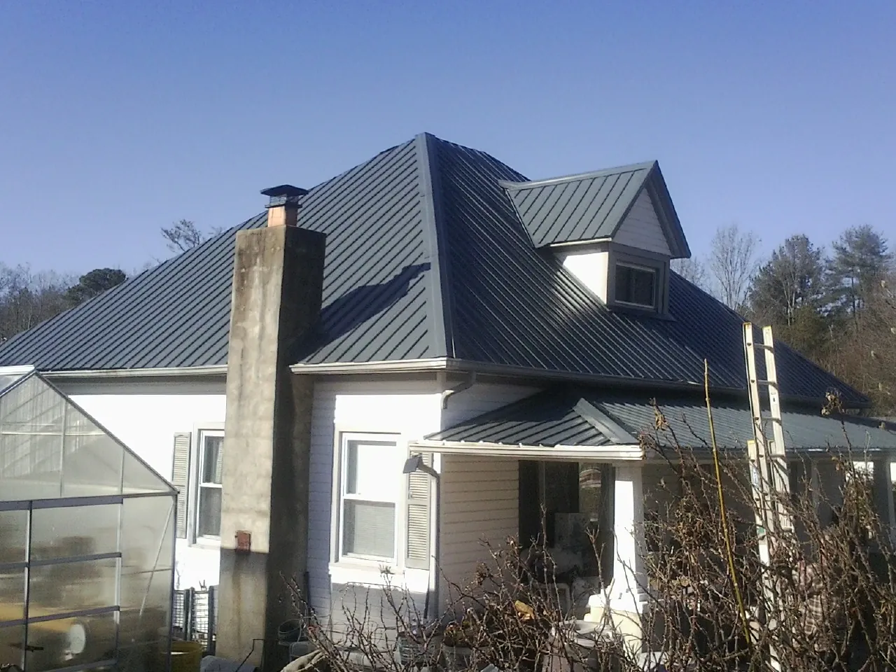 Dark blue standing seam metal roof on a white farmhouse with dormer — Slate & Tile Roof Repair by Roofing Brothers in Sula