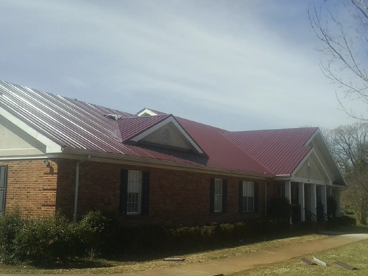 Red metal roof with gabled entries on a long brick building, from a Hail Damage Roof Repair job in Sula