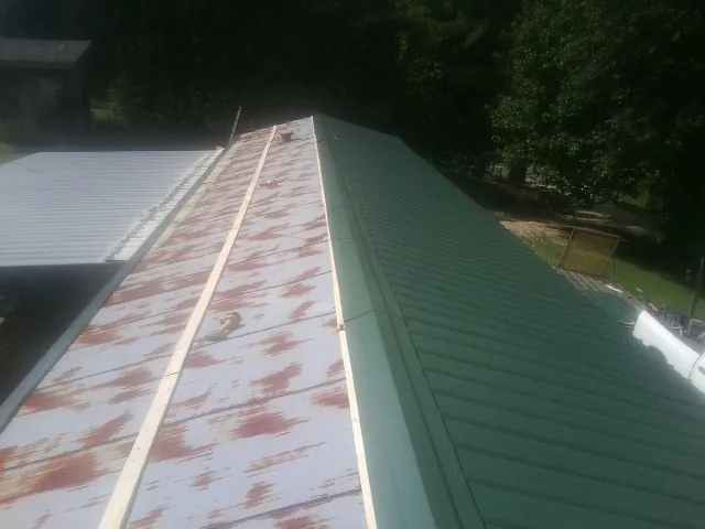 Old rusted panels beside newly installed green metal roofing — Wind Damage Roof Repair by Roofing Brothers in Sula