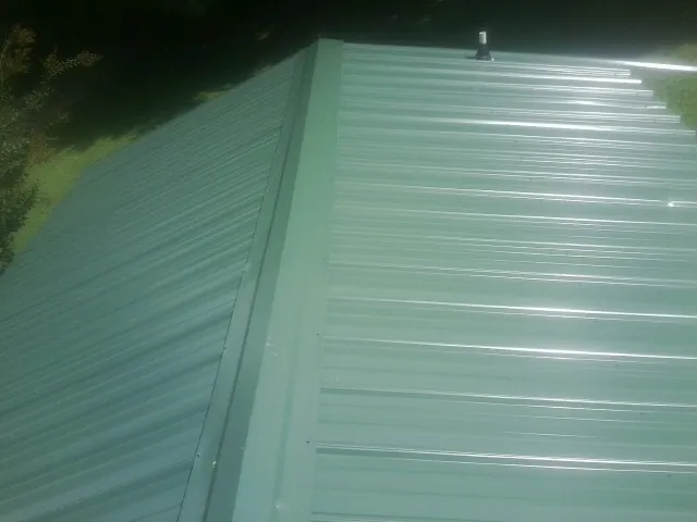 New green metal panels meeting at the ridge of a roof — Flat Roof Repair work by our crew in Sula